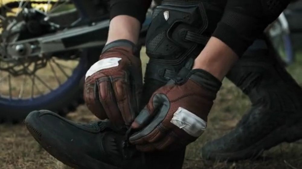 Motorcyclist lacing up protective riding boots with gloves on, preparing for a ride